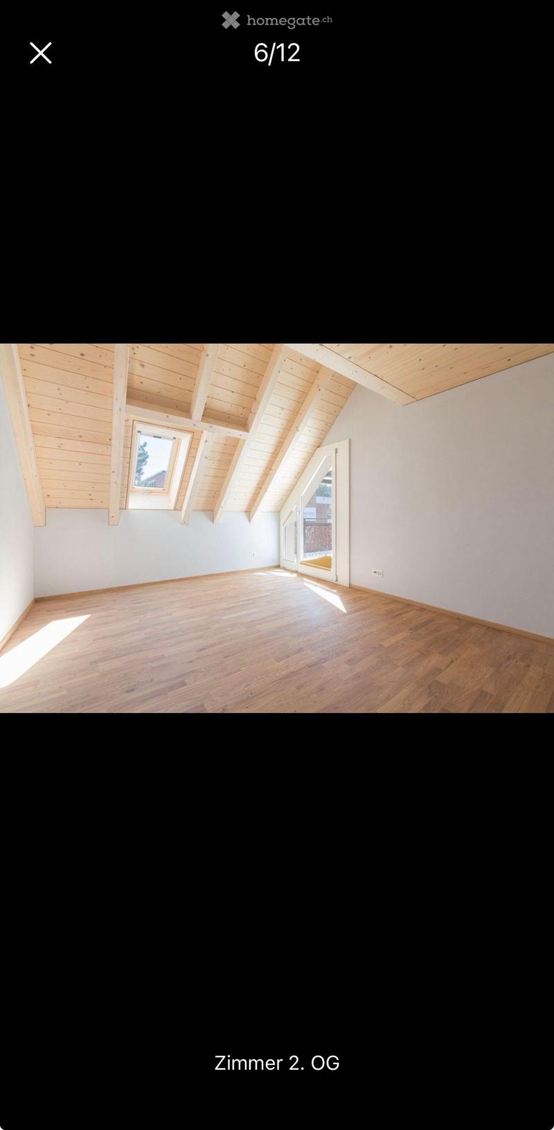 Empty room with wooden floor, white walls, and exposed wooden ceiling beams. Features large windows and a sliding glass door leading outside.