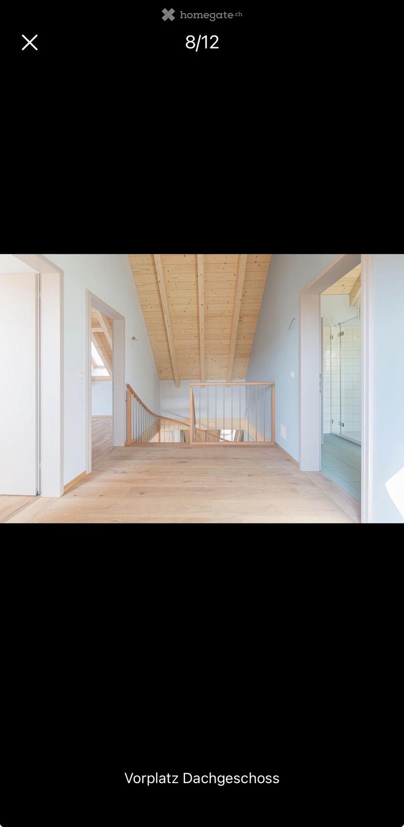 Bright hallway with wooden flooring, light blue walls, exposed wooden ceiling beams, and a metal railing leading to an upper level.