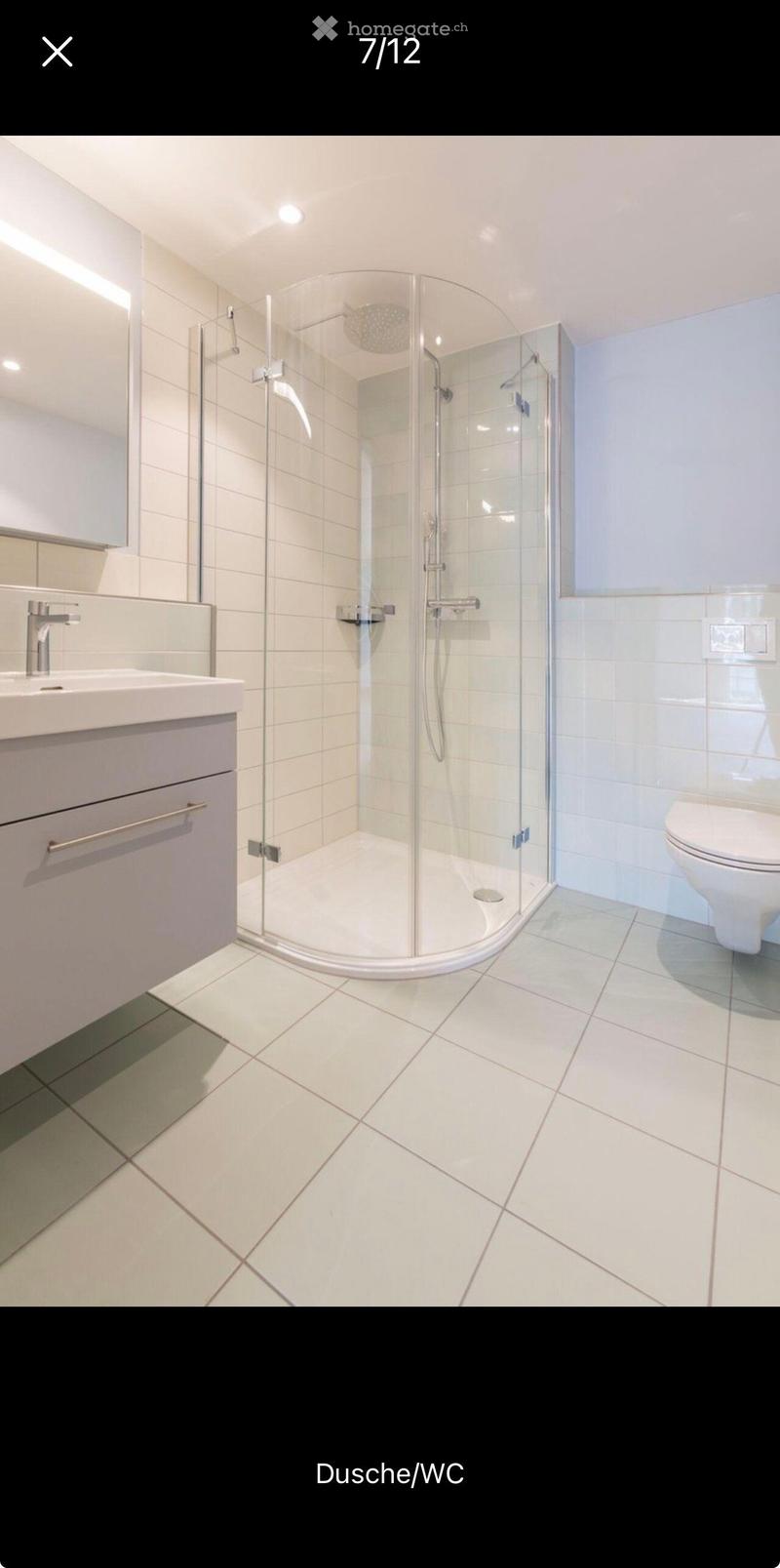 Modern bathroom with white tiles, a corner shower with glass enclosure, a sink with a chrome faucet, and a toilet.