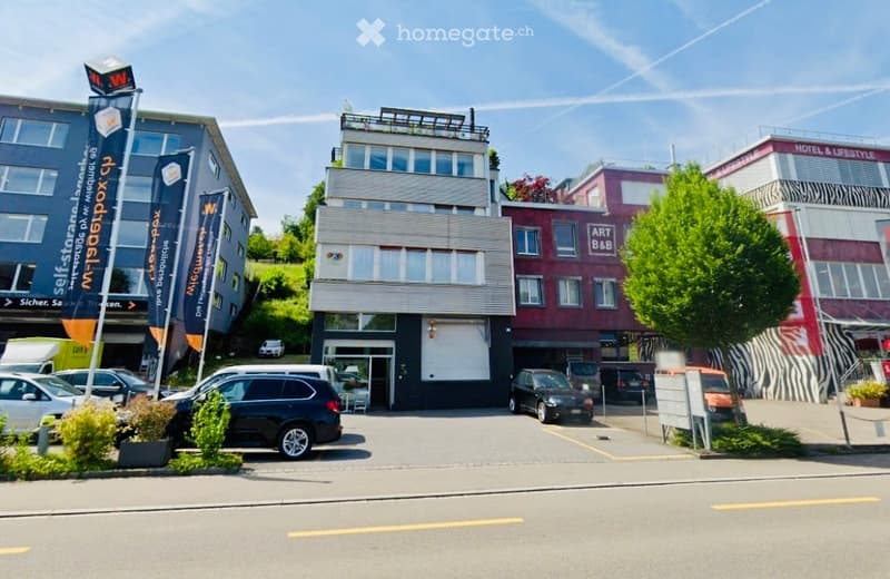 A multi-story commercial building with modern architecture, featuring large windows, signage for 'selfstorage', and a parking area with several cars.
