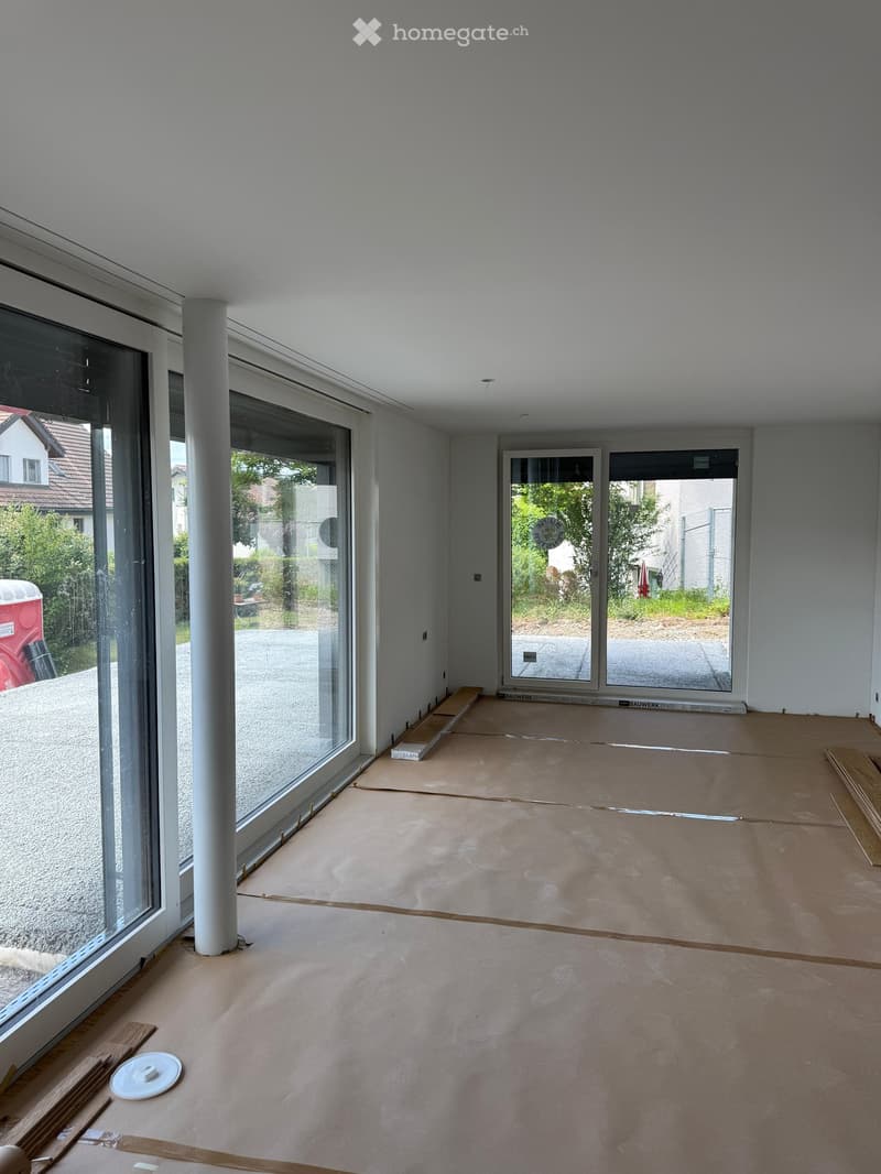 Empty room with light grey walls, large glass windows, and a smooth, unfinished floor. No furniture or equipment is present.