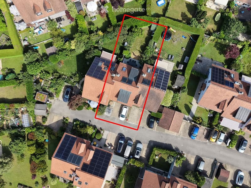 Aerial view of a residential house with a tiled roof, solar panels, and a driveway with parked cars.