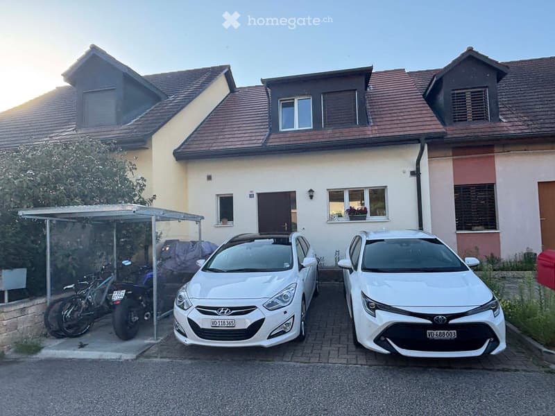 House. Two-story house with a tiled roof, multiple windows, and a covered parking area with two cars and a motorcycle.