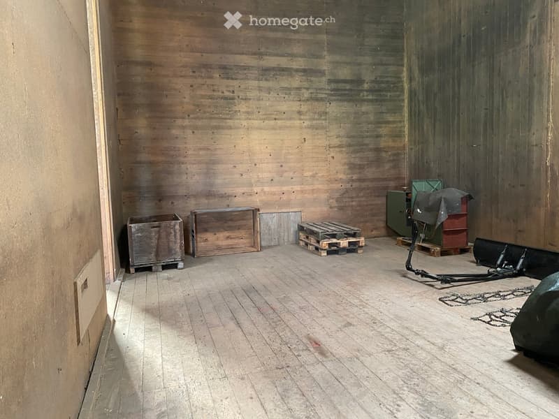 Empty wooden room with bare walls and floor, featuring a few storage crates and pallets in the corner.