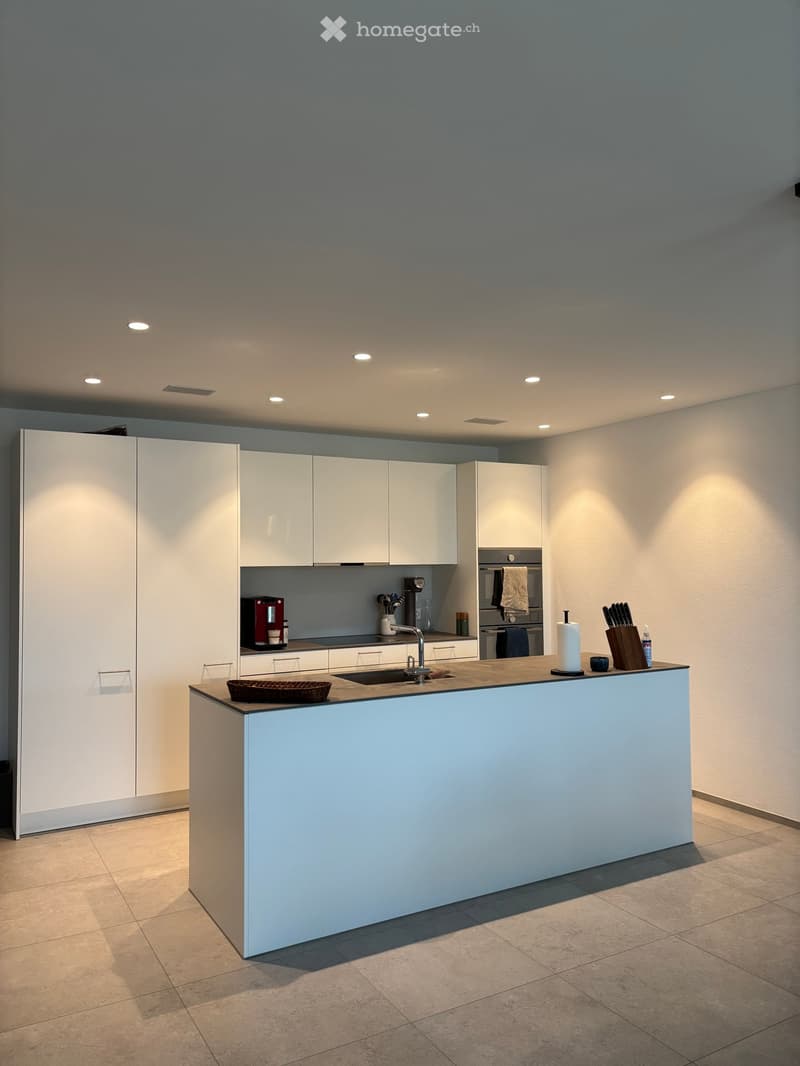 Modern kitchen with white cabinets, a central island, and various appliances including a coffee maker and knife block.