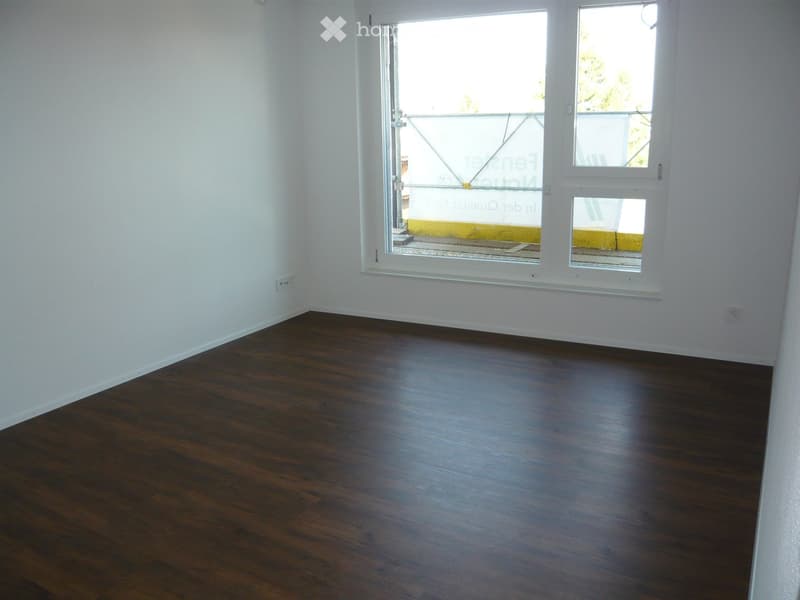 Empty room with dark wooden flooring and white walls, featuring large windows and a sliding door leading to a balcony.