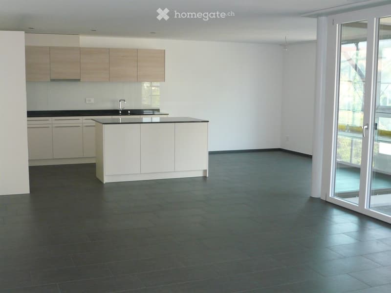 Empty kitchen with white cabinets, black countertops, and dark tiled flooring. Large glass sliding doors lead to an outdoor area.