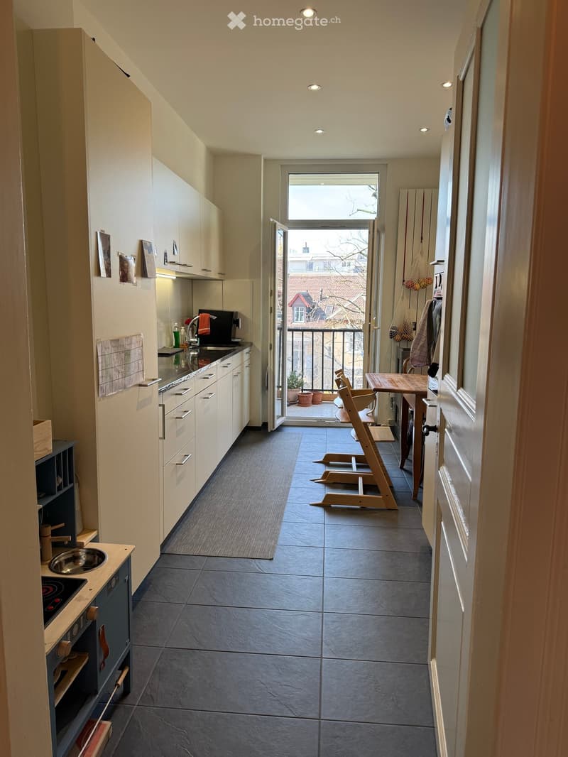 Modern kitchen with white cabinets, dark tiled floor, and a small balcony area with a table and chairs.