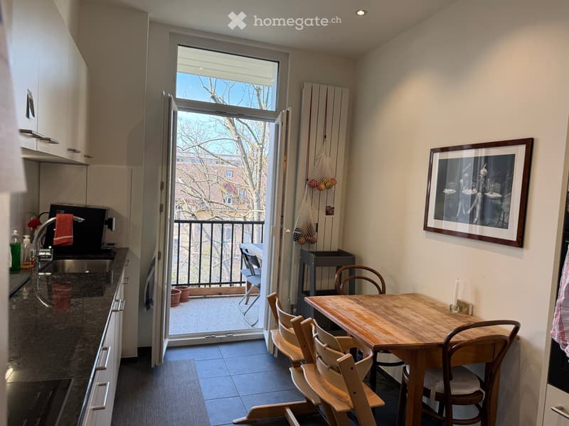 Modern kitchen with a dining area, open to a balcony, equipped with a sink, oven, and a small dining table with chairs.
