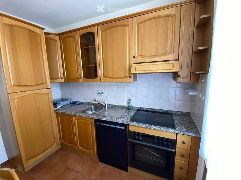 A compact kitchen with wooden cabinets, granite countertops, a stainless steel sink, and built-in appliances including a refrigerator, oven, and dishwasher.