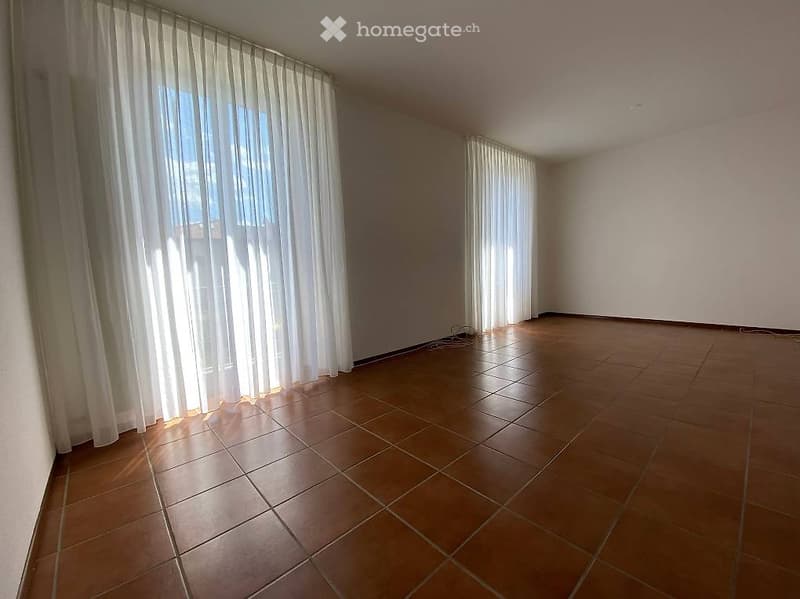 Empty room with tiled floor and large windows covered by white curtains. No furniture or equipment present.