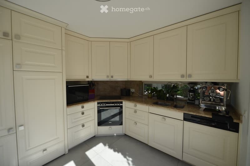 Modern kitchen with white cabinets, granite countertops, built-in oven, and a coffee machine.