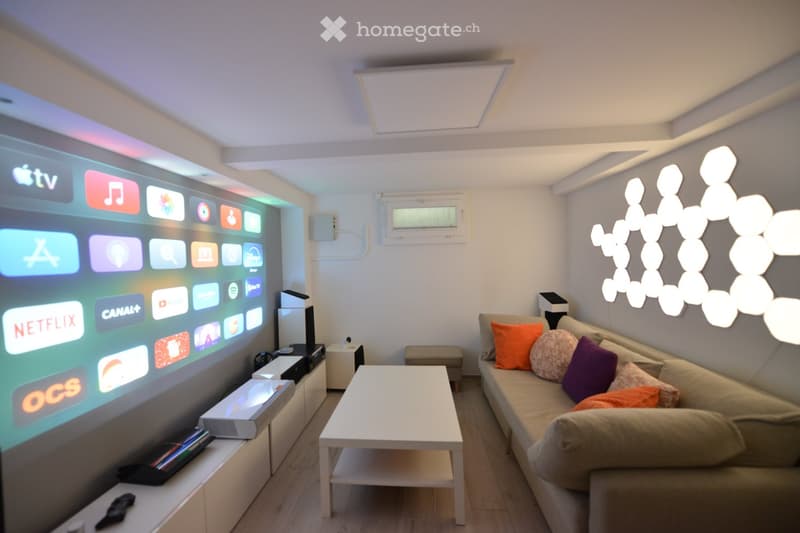 Modern living room with a large projector screen, a white coffee table, a beige sofa with colorful pillows, and a white entertainment center.