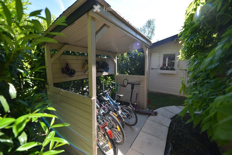 A wooden shed with bicycles, a scooter, and helmets hanging on the wall.