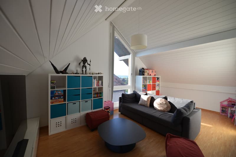 A cozy living room with a couch, coffee table, and storage boxes. Bookshelves and toys are neatly arranged. A lamp hangs from the ceiling.