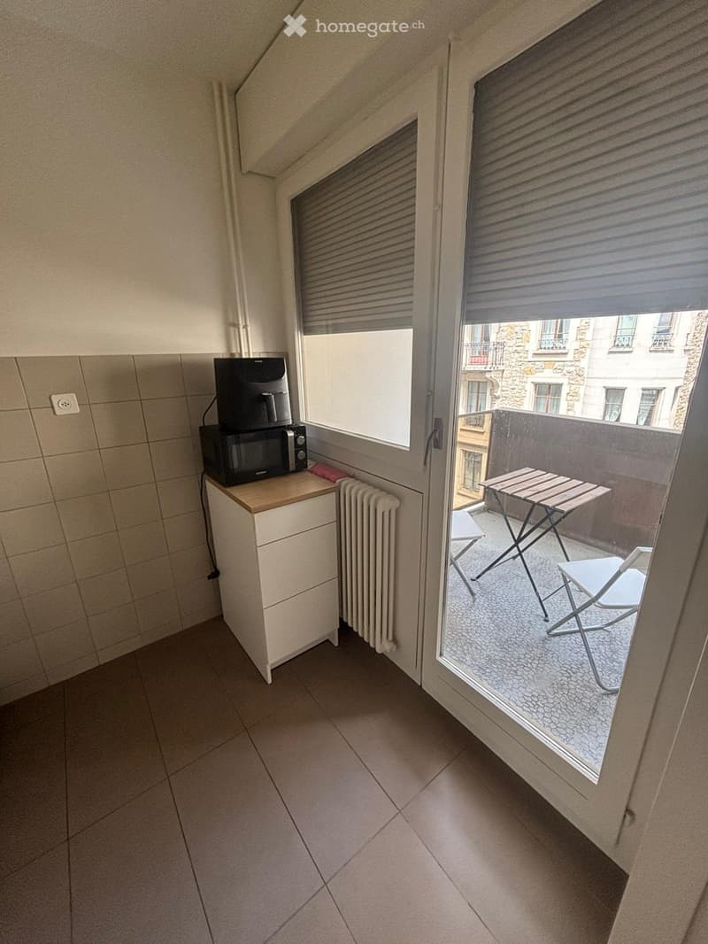 Balcony with a small table and chairs, microwave on a cabinet, radiator, and a view of the city.