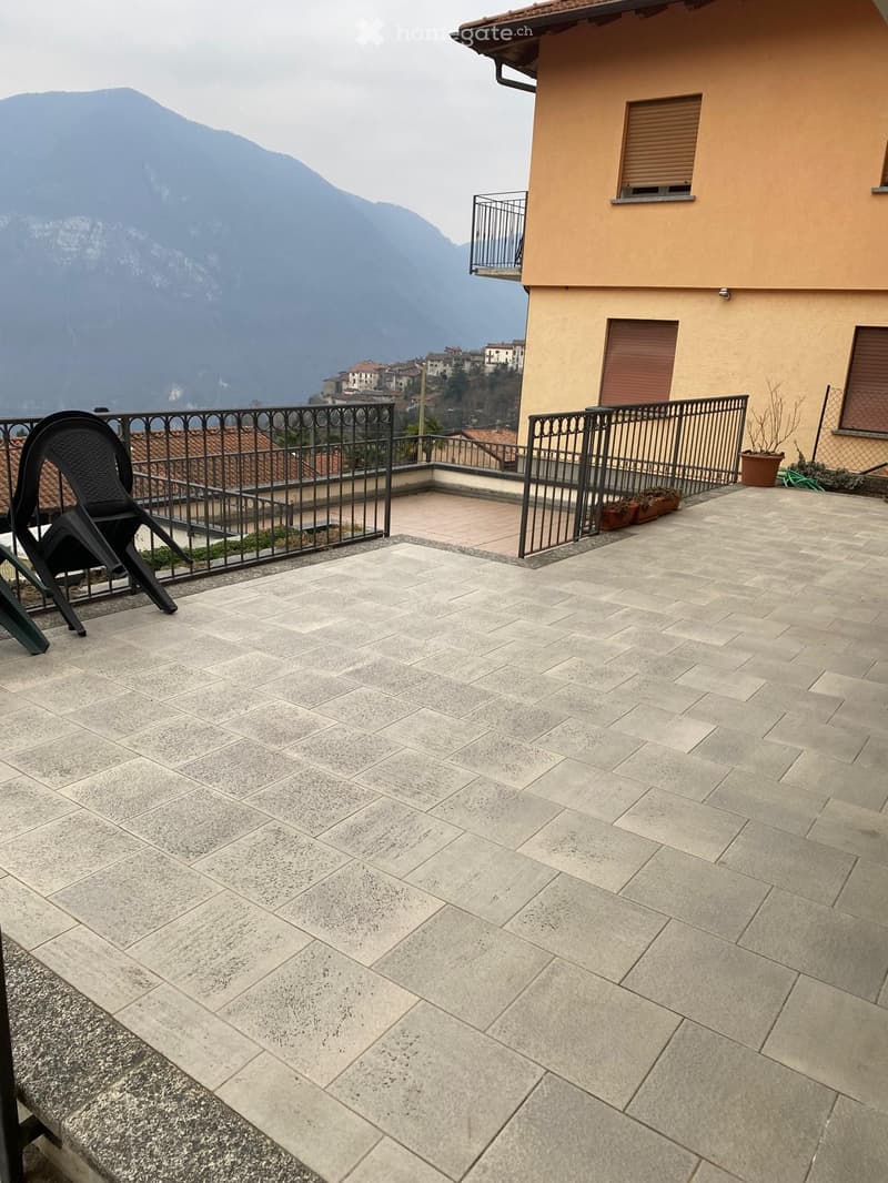 Balcony with stone tiles, metal railing, and a view of mountains and town.