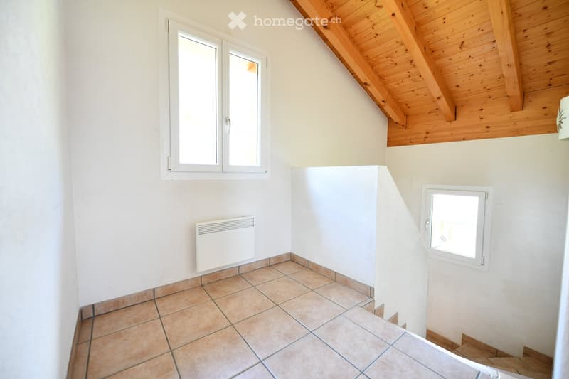 Empty hallway with tiled floor, white walls, wooden ceiling, and two windows, one with a radiator below it.