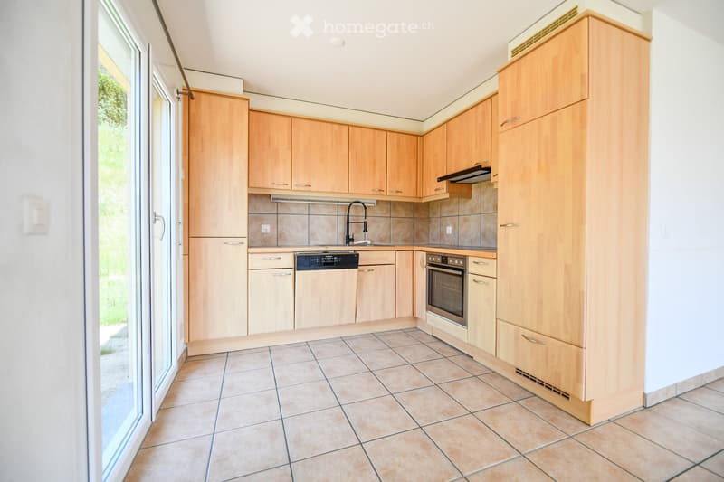 Modern kitchen with light wooden cabinets, tiled floor, and built-in appliances including an oven and dishwasher.