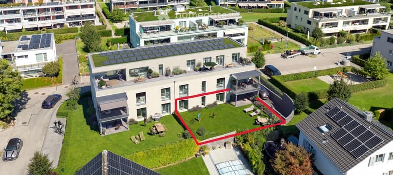 Aerial view of a residential complex with multiple modern houses, green lawns, balconies, and parking areas.