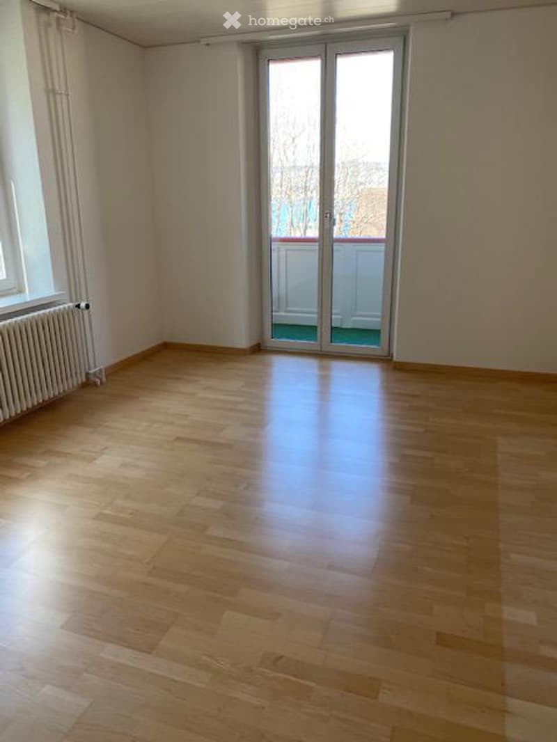 Empty room with wooden flooring, large window, and sliding glass door leading to a balcony.