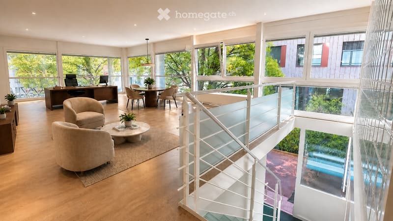 Modern, open-concept living and dining area with large windows offering a view of greenery. Features include a sofa, coffee table, dining table with chairs, desk with computers, and potted plants.
