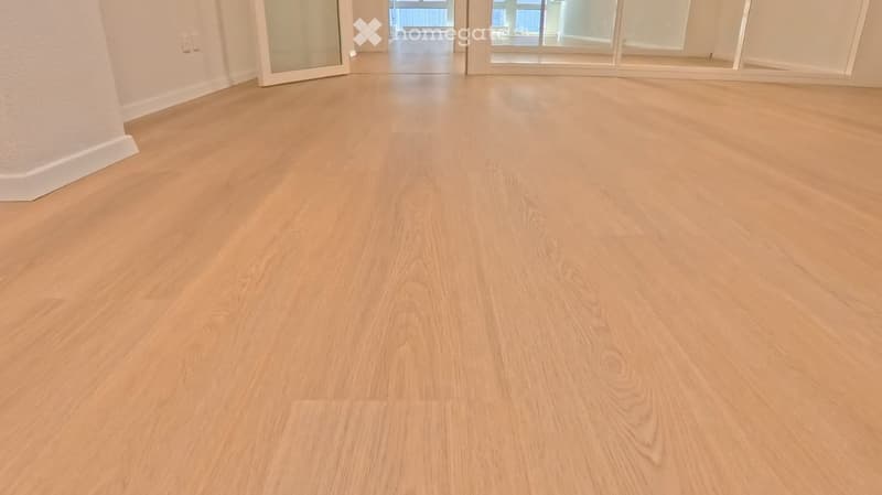 Empty room with light wooden flooring, white walls, and large glass doors leading to another space.