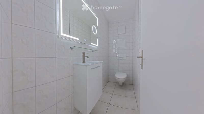 Modern bathroom with white tiles, a white sink cabinet, a mirror with LED lighting, and a toilet.