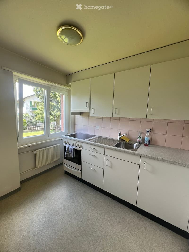 Bright kitchen with white cabinets, a sink, an oven, and a window offering a view of greenery outside.