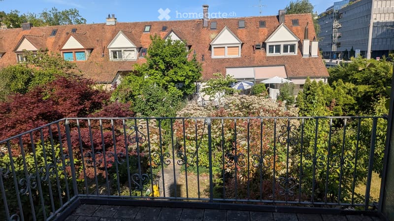 Balcony overlooking a garden with various trees and shrubs, featuring a metal railing with decorative scrollwork.