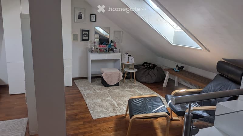 Cozy attic room with wooden floors, slanted ceilings, and skylights. Features a leather sofa, wooden chair, small bench, vanity table, and decorative items.