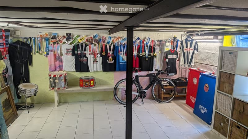A room with tiled flooring and a variety of sports memorabilia, including medals, t-shirts, a bicycle, and drums.