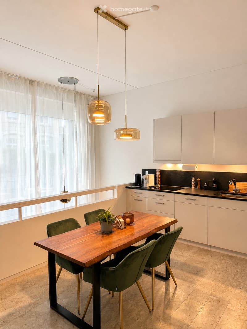 Modern kitchen with white cabinets, a wooden dining table, green chairs, pendant lights, and a view through large windows.