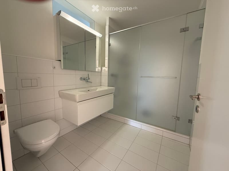 Modern bathroom with white tiles, a toilet, a sink with a modern faucet, a large mirror, and a glass shower enclosure.