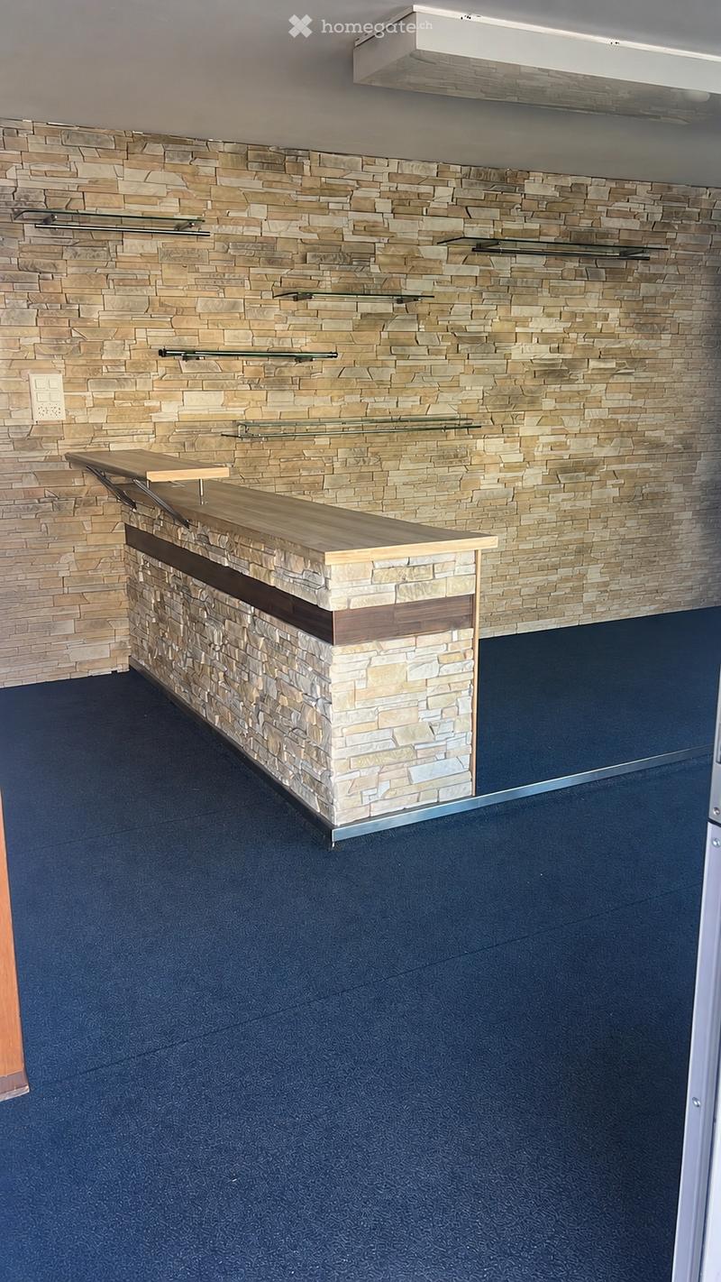 Reception area with a stone wall backdrop, a wooden reception desk, and glass shelves mounted on the wall.