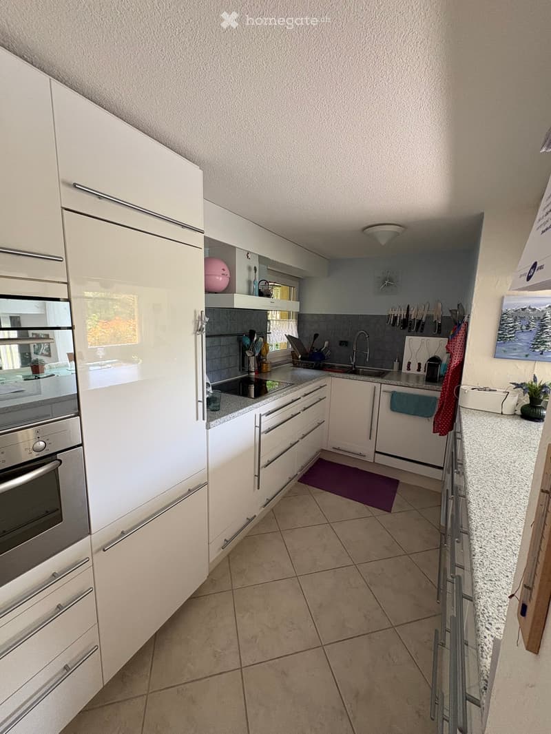 Modern kitchen with white cabinets, stainless steel oven, granite countertop, and various kitchen utensils. Features a sink with a modern faucet, a clock on the wall, and a small plant on the counter.