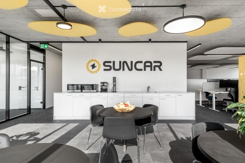 Office space with modern furnishings, white cabinets, central table, kitchen appliances, decorative lighting, and minimalist decor.
