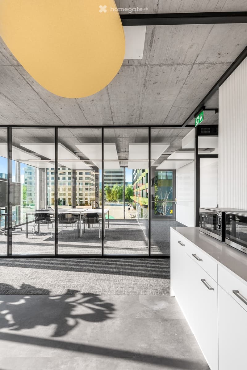 glass walls, white countertops, round yellow ceiling light, table, chairs, view of trees and buildings
