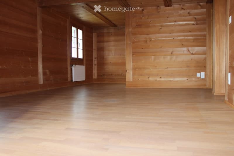Empty wooden room with wooden walls, ceiling beams, and a window. No furniture or equipment present.