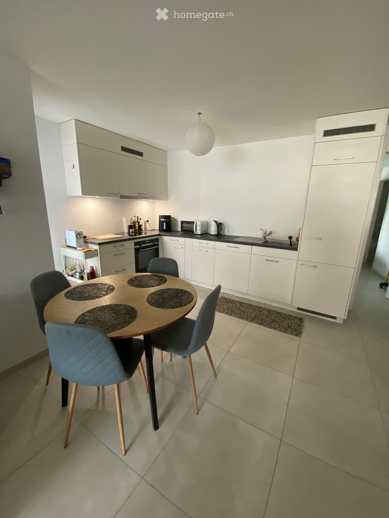 Modern kitchen with white cabinets, a dining table with four chairs, and various appliances including an oven, microwave, and coffee maker.