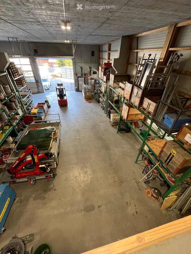 Large open space with shelves and industrial equipment, concrete floor, two forklifts parked, metal racks with various storage boxes, doors leading to outside and other rooms