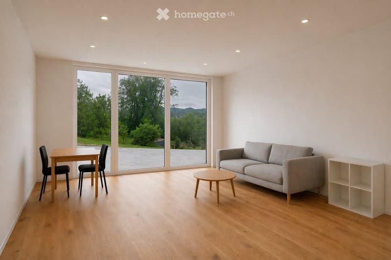 Modern living room with light wooden flooring, large windows overlooking a green landscape, a grey sofa, a round coffee table, a dining table with chairs, and a white shelving unit.
