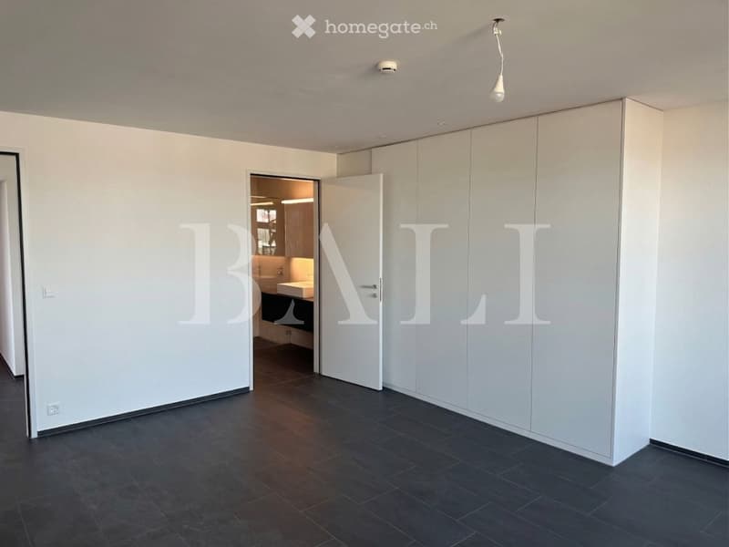Empty room with white walls, black tiled floor, large white wardrobe, open door leading to a bathroom with a sink and a toilet.