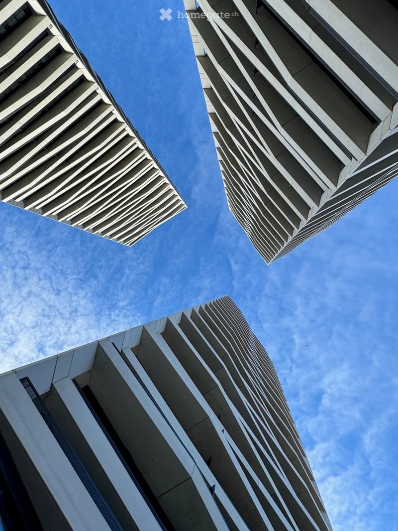 Three modern high-rise buildings with a wavy pattern on their facades, under a blue sky with scattered clouds.