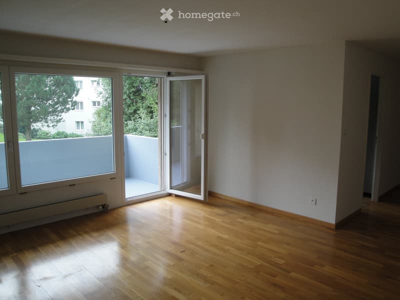 Empty room with wooden flooring, large windows, and an open sliding door leading to a balcony area.