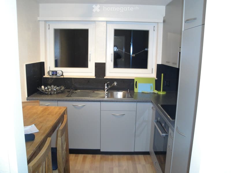 Modern kitchen with white cabinets, stainless steel sink, wooden table, and various appliances.