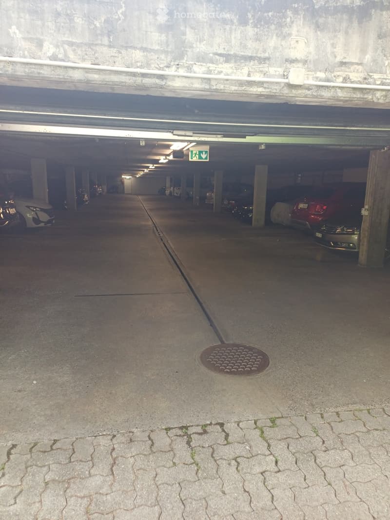 Underground parking area with several parked cars, concrete pillars, and a visible emergency exit sign.
