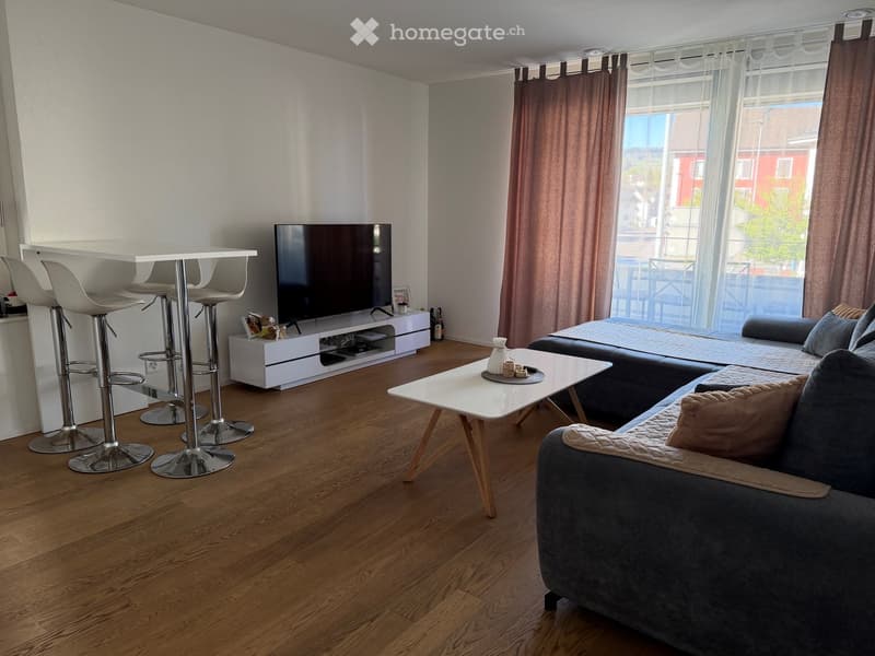 Modern living room with wooden flooring, grey sofa, coffee table, TV stand, and bar area with stool chairs.