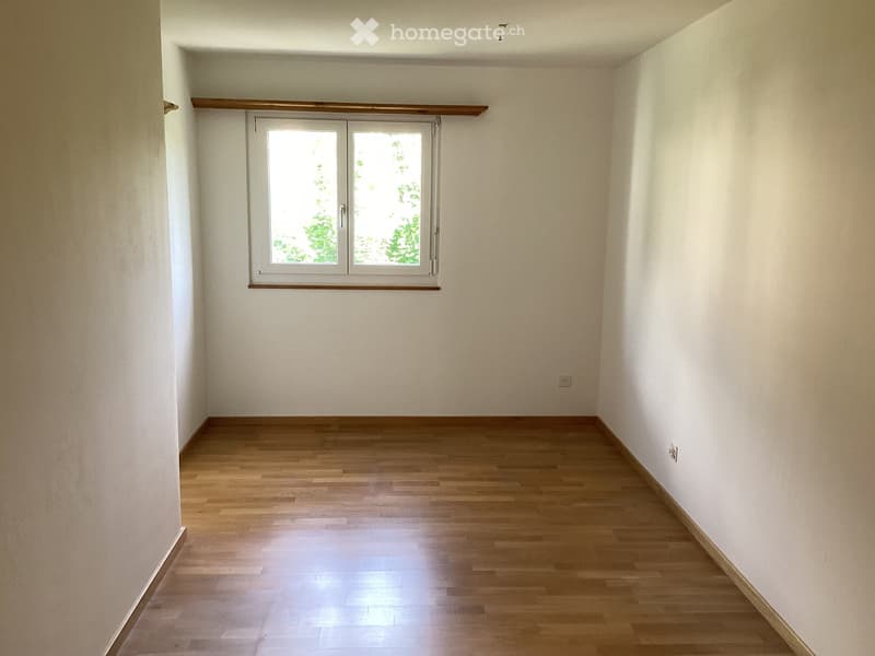 Empty room with wooden flooring, white walls, and a single window with a wooden frame and a small wooden shelf above it.