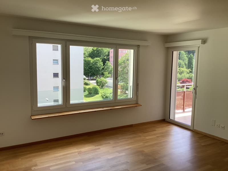 Empty room with wooden flooring, large windows, and a sliding door leading to a balcony or terrace.